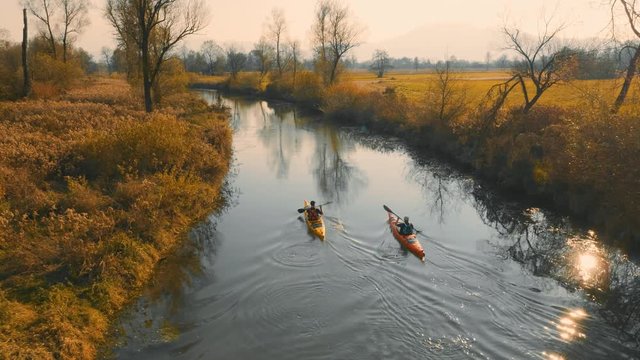 Aerial tracking shot of two kayakers paddling up the river on a beautiful autumn sunny day.

