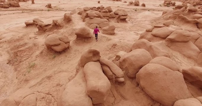 Aerial view of a man in a red jacket standing small among a maze of huge sandstone goblins in Goblin Valley in Utah. Their round forms fill the frame in a strange and solemn desert scene.