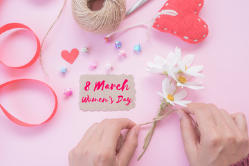 Happy International Women's Day message on brown paper inside yellow letter with handmade red heart, beautiful flowers, red ribbon and wooden heart on pink background. Womens Day concept.