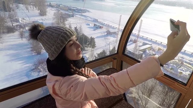 Girl doing selfie in the cockpit of a Ferris wheel on the phone smiling.