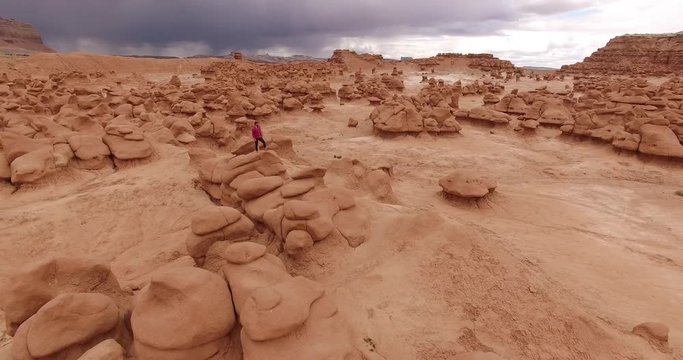 Aerial view over the whole valley of sandstone goblins in Utah with a man in red standing tiny on a ridge below a dark storm sky. A vast and brooding scene of the southern Utah desert country.