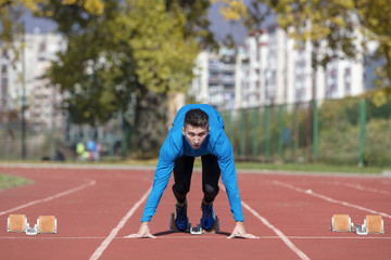 Obraz premium Man runner in blue shirt and shorts and sport shoes in steady position before run at start of race.