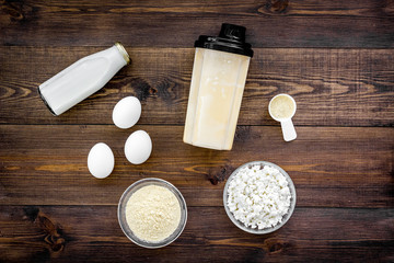 Fototapeta na wymiar Protein diet for the athlete Scoop of protein near shaker, milk, eggs, cottage cheese on dark wooden background top view