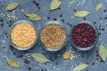 Cereal beans in glass cups: beans, peas and lentils, with spices top view.