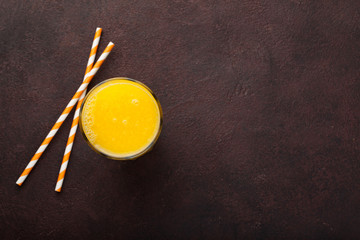 A glass of freshly squeezed orange juice and straws for juice on a dark brown background. Top view with copy space