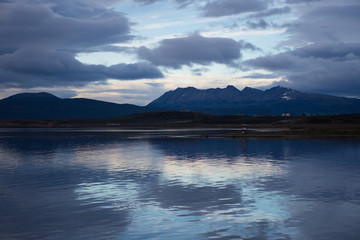 Fototapeta premium Sunset in Ushuaia with dark gray and blue clouds. A reflection of the sunset is seen in the water.
