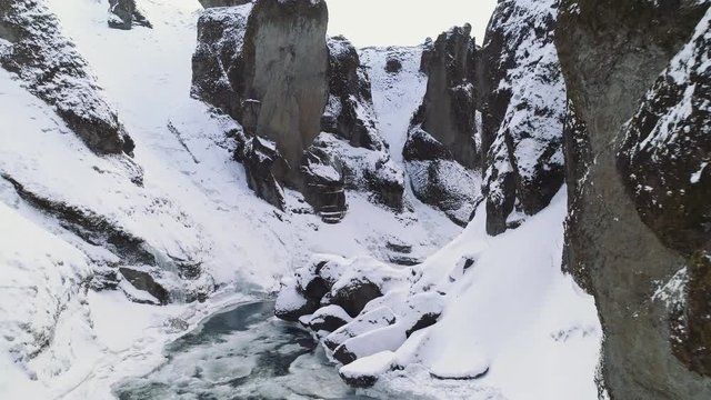 Flying through a snow covered canyon with river below: pristine winter landscape and snow. Flies over rocks and around corner to reveal scene. Icicles hanging from cliffs.