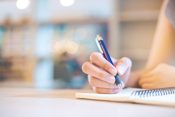Business woman hand is writing on a note pad with a pen.