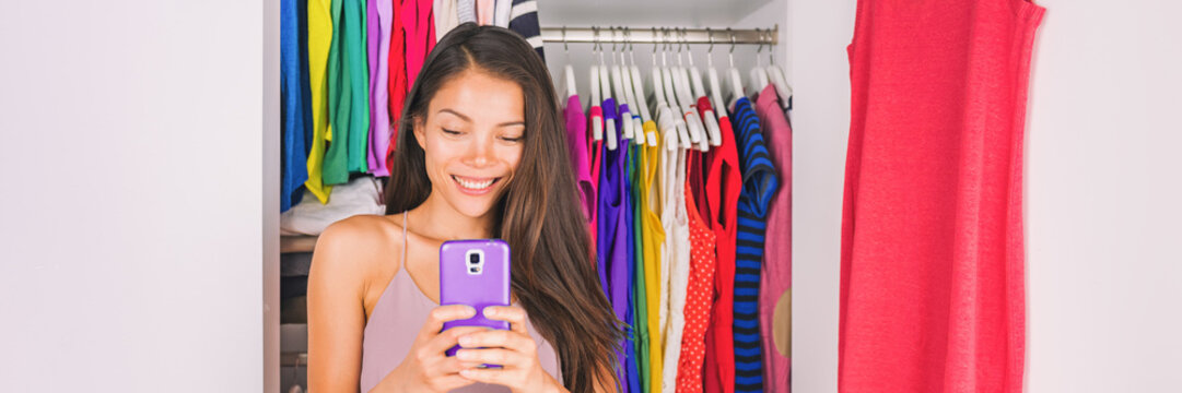Selfie Asian girl taking photo with phone of outfit in walk-in closet dressing room. Clothes fashion stylist. Shopping girl using smartphone fashion app posting on social media. Banner panorama.