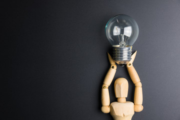 Wooden dummy toy and light bulb on black background with copy space.