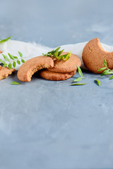 Cookies with bite marks and tiny green leaves decor on a stone background with white linen napkin. Spring baking concept with copy space. Breakfast still life.