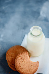 Cookies with bite marks and a bottle of milk on a light blue kitchen table with copy space. Healthy breakfast minimalist concept.