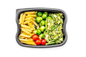 Healthy and hearty lunch for office worker. Vegetables Brussels sprout, cherry tomatoes, knock beans near pasta in plastic container on white background top view