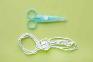 Cyan Plastic children safety scissors with rope on green background.