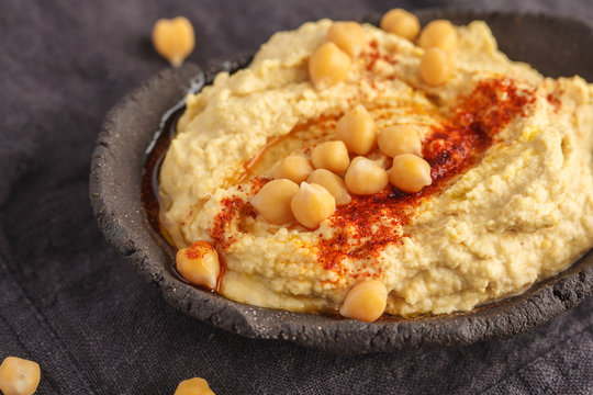 Homemade traditional hummus in a clay dish, dark background, top view. Healthy vegan food concept.