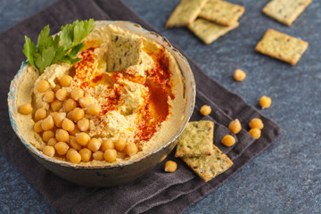 Homemade traditional hummus with crackers in a clay dish, dark background, top view. Healthy vegan food concept.