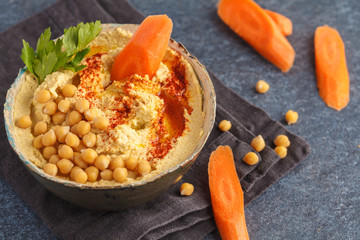Homemade traditional hummus with carrots in a clay dish, dark background, top view. Healthy vegan food concept.
