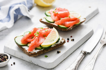 Salmon toast with cream cheese and cucumber on white cutting board, closeup view. Healthy snack, appetizer or breakfast
