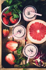 Pink fresh smoothies with grapefruit, strawberry and pomegranate in wooden tray, top view, selective focus, toned image. Healthy lifestyle, detox, dieting, clean eating, vegan, vegetarian concept