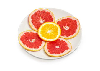 Round slices of red grapefruits and orange on white dish