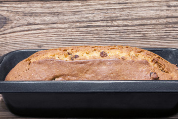 Homemade rectangular traditional cupcake with raisins in baking dish on the brown wooden background. Closeup, selective focus