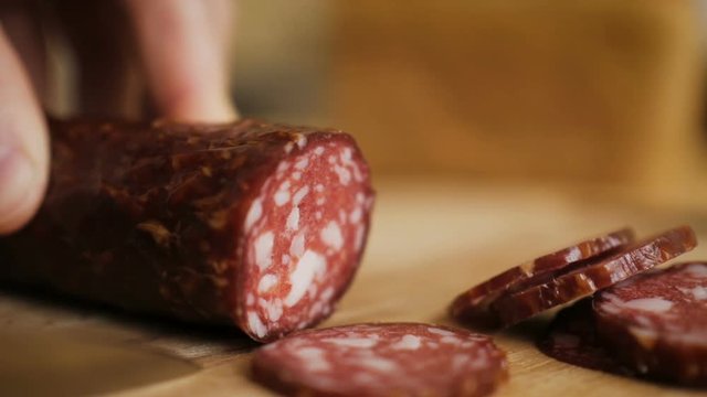 Man cuts into thin slices fatty sausage. Shooting closeup. Chef cutting salami with a knife on a wood board close up.