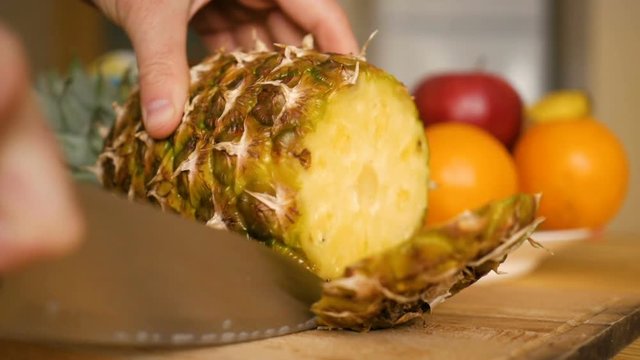Man slicing  ananas , pineapple with knife on wooden board with fruits and vegetables on background. Close-up.