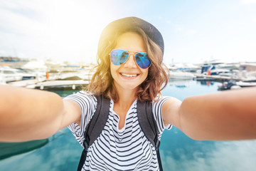 young beautiful woman traveler in a hat makes selfie on a smartphone on a beautiful port background...