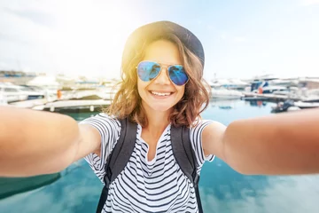Papier Peint photo Chypre young beautiful woman traveler in a hat makes selfie on a smartphone on a beautiful port background on a sunny day by the sea. Vacations, adventures and sea voyages