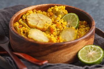 Curry bulgur with vegetables in wooden bowl. Dark background, vegan meal concept.