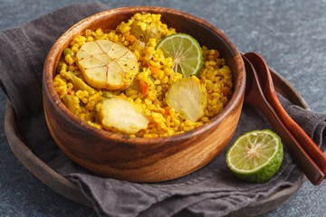 Curry bulgur with vegetables in wooden bowl. Dark background, vegan meal concept.