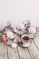 tea set in composition with flowers and marshmallows. Coffee mug on a saucer, a teapot and a sugar bowl. Filmed in the interior