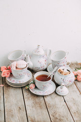 tea set in composition with flowers and marshmallows. Coffee mug on a saucer, a teapot and a sugar bowl. Filmed in the interior