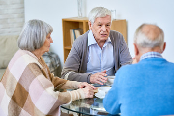 Obraz premium Group of senior friends enjoying tea time meeting at home and sharing memories, focus on white haired senior man talking and gesturing