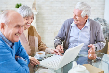 Portrait of three modern senior people using laptop in retirement home and smiling happily, copy...