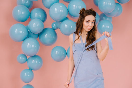 A tender girl in a blue dress, in a pink room playing a blue ribbon