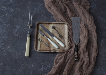 on a wooden plate a vintage fork, knife, spoon, fork. Near the plate is a large fork and a crochet for the cake - cutlery