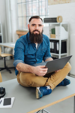 Bearded man sitting on office desk with laptop