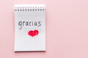 Word Thank you in a notebook in spanish on a pink background