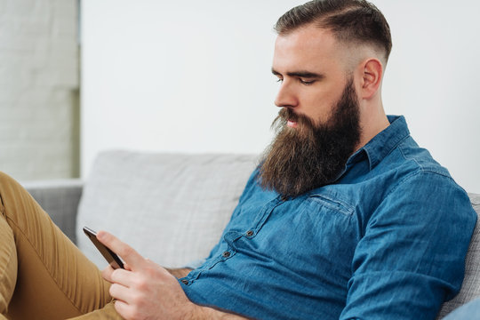 Bearded man with mobile phone sitting on sofa