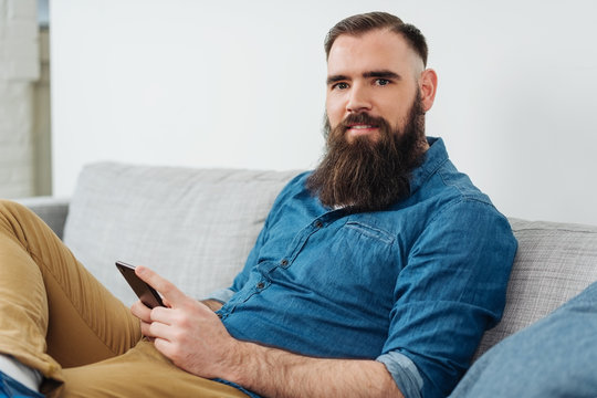 Smiling bearded man with mobile phone on sofa