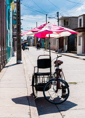 Obraz premium Bicycle taxi, pedicab bike parked on the side of a street. Colorful umbrella attached to the cart to provide shade for riders.
