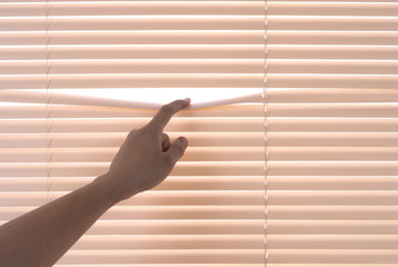 Windows jalousie,hand separating slats of venetian blinds with a finger to see through