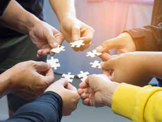 Closeup image of many people hands holding a jigsaw puzzle piece in circle together with sunlight effect.