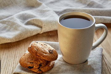 Porcelain teacup with chocolate chips cookies on cotton napkin on a rustic wooden background, top view