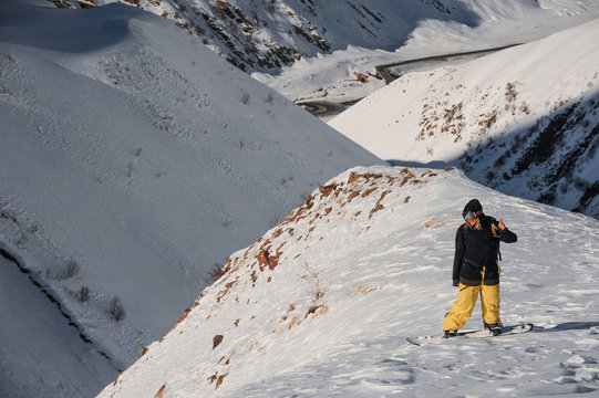 Freeride male snowboarder standing on the mountain peak