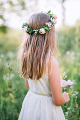 Naklejka premium girl in white dress with back on head wearing a wreath of pink roses and standing on a green garden