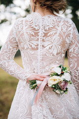 close-up of a bride's back in a lace dress with buttons that holds a bouquet of roses
