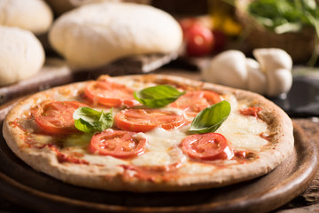 Italian pizza with tomato topped with melted golden cheese, herbs and basil served on a round wooden board on an old wood table