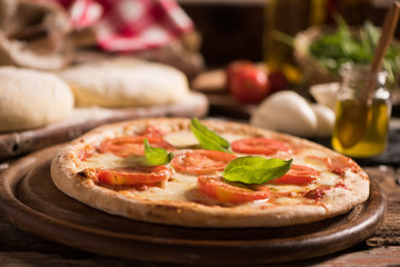 Italian pizza with tomato topped with melted golden cheese, herbs and basil served on a round wooden board on an old wood table